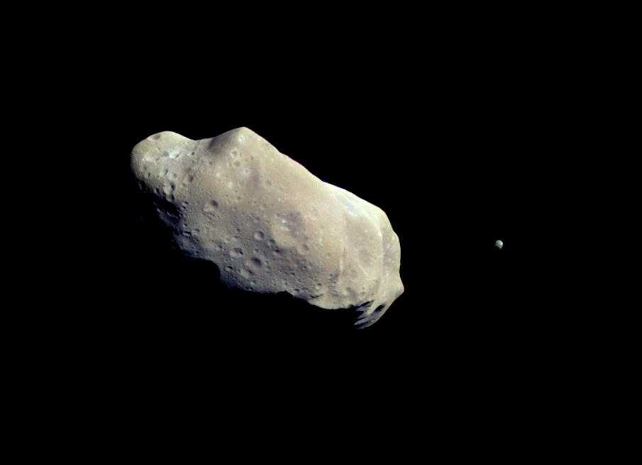 The asteroid Ida is an odd-shaped object with craters on its surface. From the picture, one cannot tell its size. On the right a small object is visible near the asteroid - its moon Dactyl.